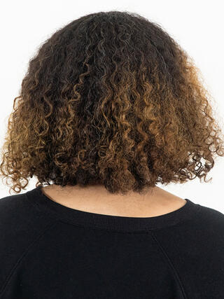 Before Photo: rear view of woman with short curly black hair with grown out roots before colour.